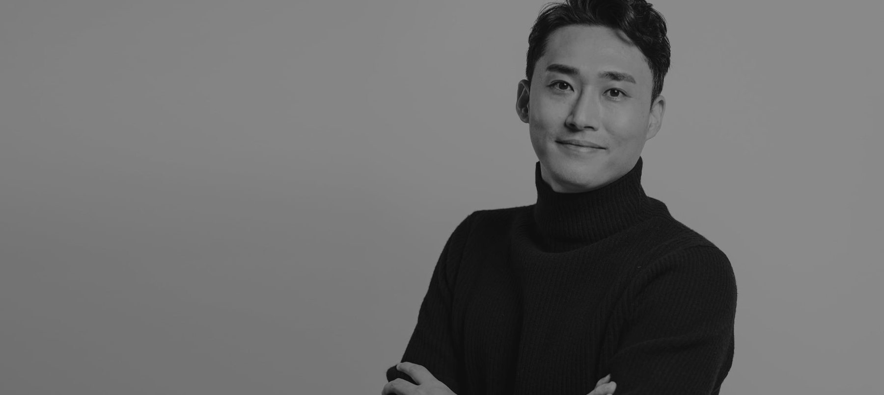 팔짱 낀 검은 터틀넥의 김용현 대표원장 흑백 사진(왼쪽 절반은 빈 회색 배경)