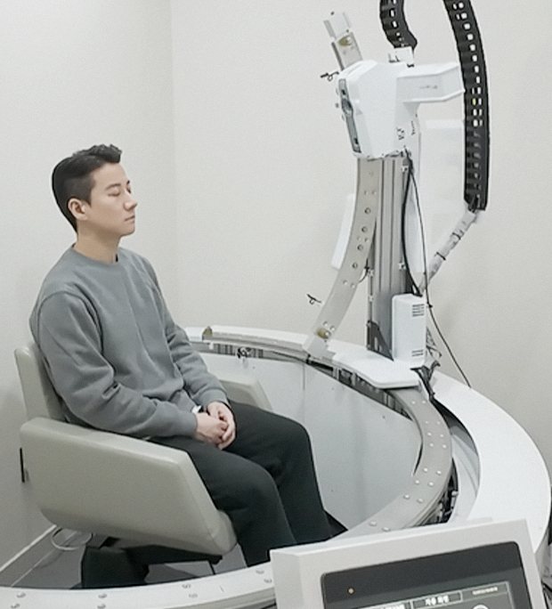원형 레일의 자동화 3D 스캐너 안에 앉아 촬영하는 남성